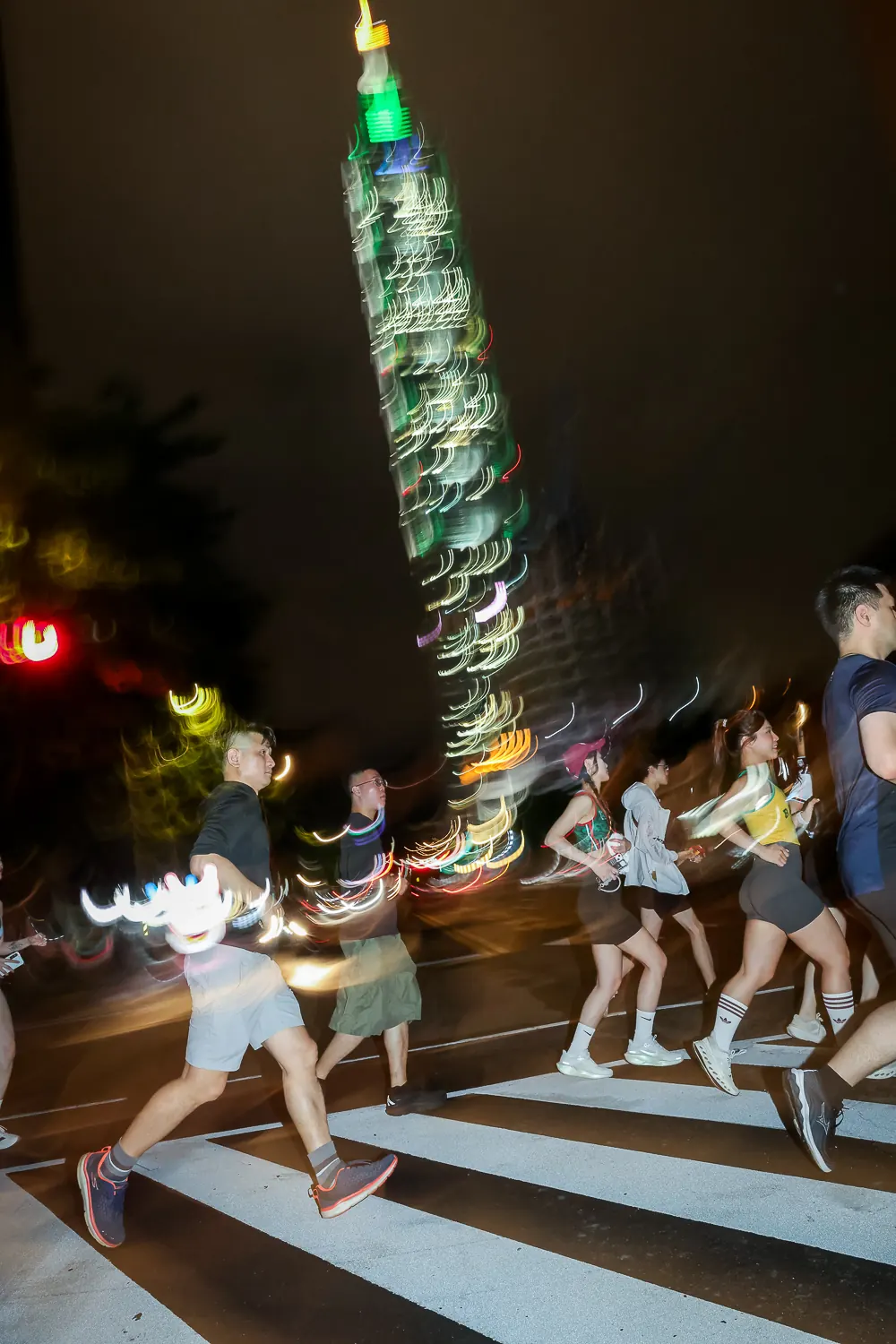 夜晚跑者穿越斑馬線，後方是點燈的台北 101，畫面帶有動態模糊。
